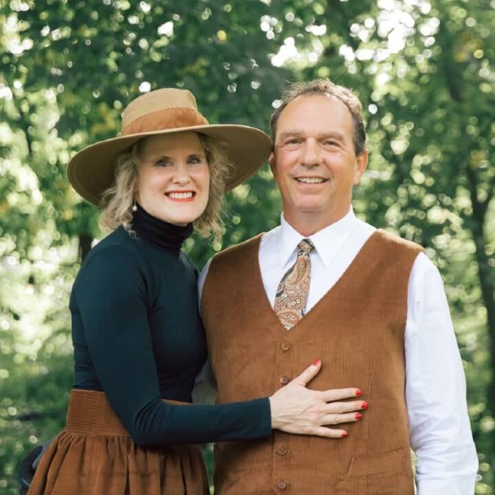 A man and woman stand together outdoors, both smiling as though sharing a cherished story. She wears a brown hat and dress, while he sports a brown vest with a tie. Green trees gently frame them in the background. – OmegaStrap – World’s Greatest Ratchet Strap A man and woman stand together outdoors, both smiling as though sharing a cherished story. She wears a brown hat and dress, while he sports a brown vest with a tie. Green trees gently frame them in the background. - OmegaStrap - World's Greatest Ratchet Strap